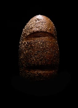 Top view of freshly baked loaf of bread with seeds placed on black background in dark studio with dim light