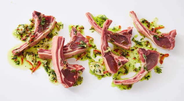 Top view of fresh raw lamb chops in marinate with oi and greens placed on white background in light kitchen