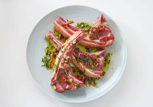 Top view of uncooked lamb chops covered with marinate with chopped greens placed on plate on white background in kitchen