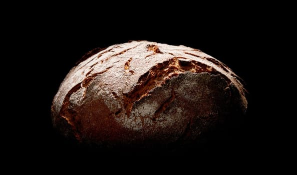 Freshly baked round loaf of bread with flour and crispy crust placed on black background in dark studio with dim light