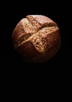 Top view of freshly baked whole loaf of full grain bread with crispy crust placed on black background in dark studio
