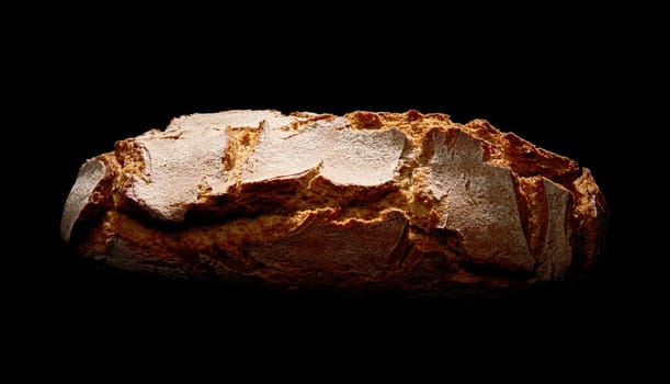 Loaf of freshly baked brown loaf of bread with crispy crust placed on black background in studio with dim illumination
