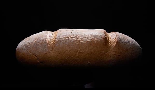 Loaf of tasty freshly baked brown Kasseler bread with crispy crust placed on black background in studio with dim illumination