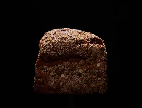 Loaf of tasty freshly baked wholegrain bread with various seeds placed on black background in dark studio with dim light