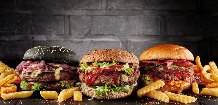 Appetizing various burgers and French fries placed in row on table on dark background