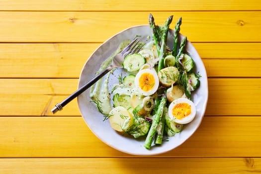 From above of appetizing spring salad with asparagus and eggs and potatoes served for lunch on wooden table