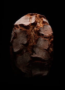 Top view of fresh tasty bread loaf with brown crispy crust placed on black background in dark studio with dim light
