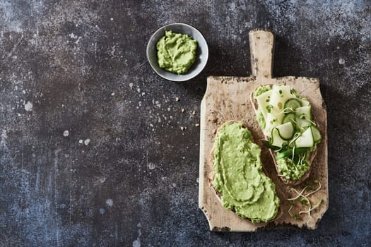 From above of appetizing toast with guacamole and cheese and cucumbers placed on wooden chopping board for vegetarian breakfast