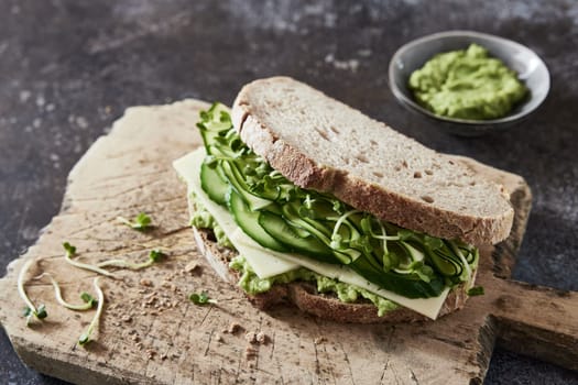From above of delicious sandwich with guacamole and cheese and vegetables placed on wooden board on table for breakfast