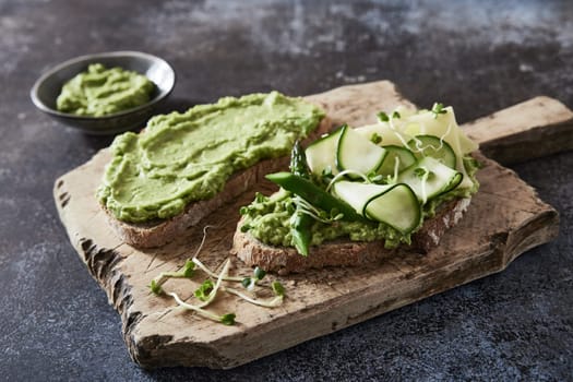 High angle of yummy vegetarian bruschettas with guacamole and cheese and cucumbers garnished with microgreen placed on cutting board