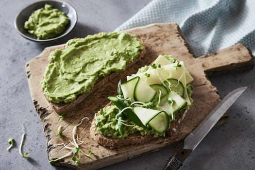 From above of delicious green toasts with guacamole and cucumbers and cheese on wholegrain bread served on wooden cutting board