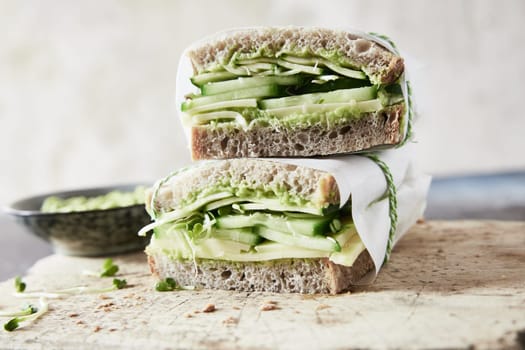 Appetizing vegetarian sandwiches with green vegetables and cheese served on wooden cutting board in domestic kitchen