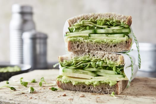 Yummy homemade sandwiches with guacamole and cheese and cucumbers placed on wooden board on table for snack