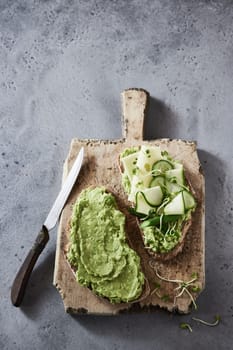 Top view of appetizing bruschettas with cheese and guacamole served with knife on wooden board on concrete table for breakfast