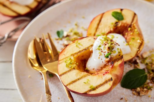 High angle closeup of sweet dessert with grilled nectarines and yogurt garnished with mint and sprinkled with pistachios placed on wooden table