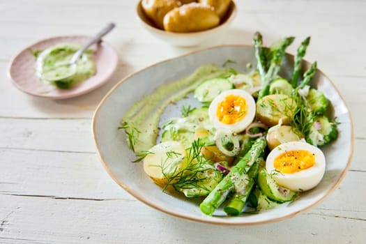 High angle of tasty salad with asparagus and eggs and potatoes served in bowl on wooden table for healthy lunch