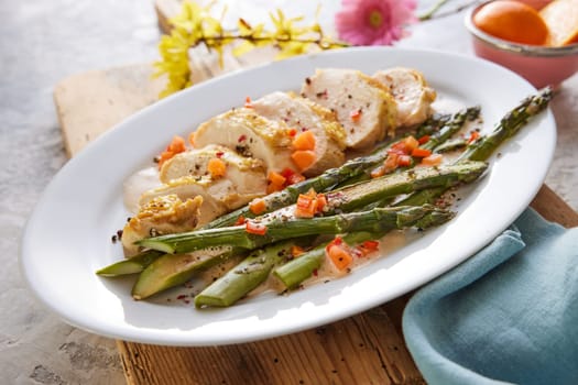High angle of plate with appetizing cut chicken breast with asparagus and carrots served on wooden board for lunch