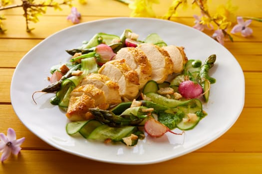 High angle of delicious cut chicken breast and healthy vegetable salad served on plate on wooden table with flowers for lunch