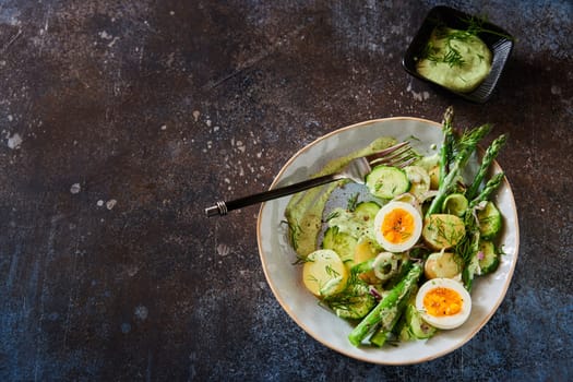 Overhead view of delicious vegetable salad with fresh asparagus and boiled eggs with potatoes served in bowl on dark concrete table