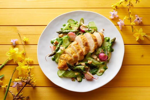 Top view of appetizing slices of chicken breast served with fresh vegetable salad on wooden table with spring flowers