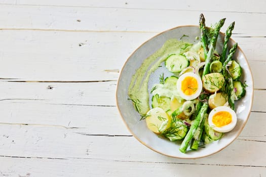 Top view of appetizing fresh asparagus salad with boiled eggs and potatoes served on plate on wooden table