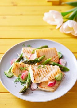 From above of tasty grilled tilapia fish with fresh vegetables served on wooden table with spring flowers
