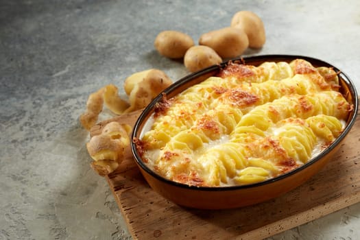 From above of yummy saucy gratin au potato baked in casserole pan and served on wooden cutting board on gray table in daylight