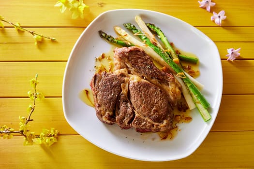 From above of appetizing rib eye steak with asparagus served on plate on wooden table with flowers