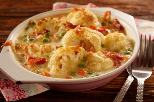 High angle of bowl with delicious cauliflower gratin with cheese placed on wooden table with cutlery