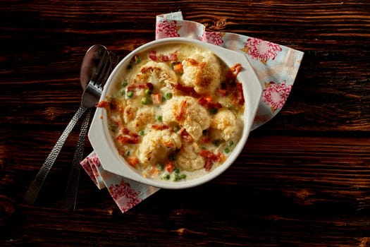 Top view of yummy cauliflower gratin with cheese and herbs served on napkin on wooden table for lunch