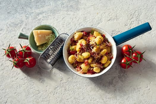 Top view of tasty potato gnocchi in pan served with ripe tomatoes and cheese on white concrete background