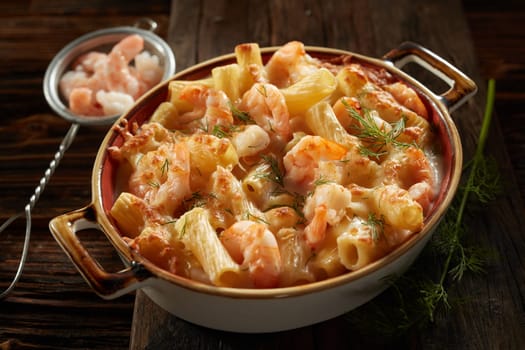 High angle of yummy rigatoni pasta with shrimps and cheese prepared in saucepan and decorated with herbs served on wooden table in kitchen