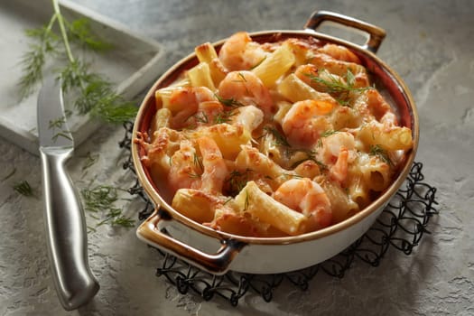 From above of appetizing creamy rigatoni pasta with prawns and dill placed on gray table near knife in kitchen