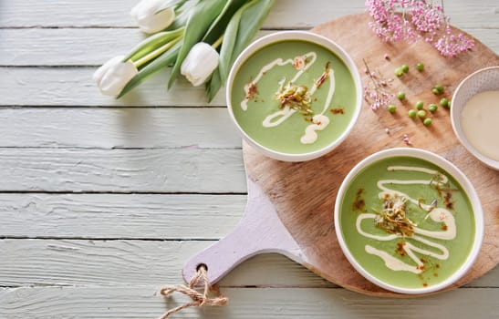 From above of delicious pea soup in bowls placed with tulip flowers on table for healthy lunch