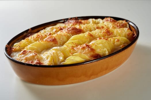 High angle of slices potatoes with cheese and crispy crust prepared in casserole pan and served on white table in kitchen