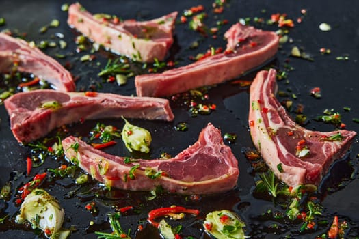 Fresh uncooked lamb chops with chopped greens and chili pepper on black background with oil and garlic in light kitchen