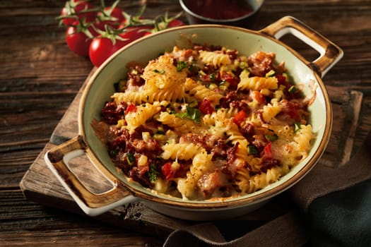 High angle of appetizing Italian fusilli baked with tomatoes minca and cheese on top in ceramic bowl on wooden board