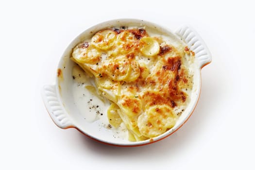 High angle of ceramic casserole an with traditional French Gratin dauphinois dish made of sliced and layered potatoes baked with cream and served on white table