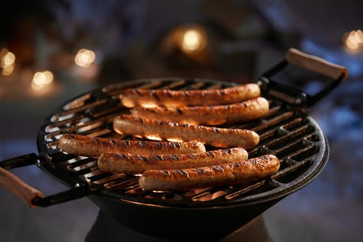 Delicious meat sausages preparing on barbecue for dinner on yard in dark winter night