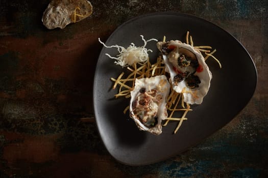 Top view of appetizing expensive open oysters served on black plate on shabby table