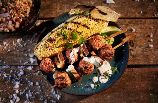 Top view of appetizing BBQ corn and meat balls on wooden sticks served with sauce and parsley leaves on wooden table with snow