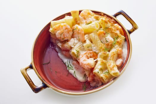 From above of appetizing rigatoni pasta baked in casserole with shrimps and creamy sauce and decorated with herbs on white table