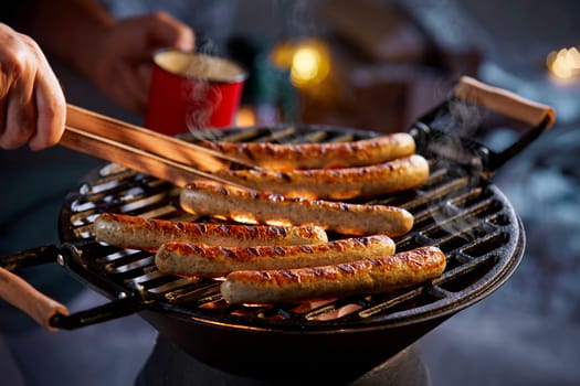 Crop anonymous male with forceps taking tasty grilled sausage from grill on barbecue at backyard at night