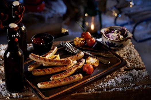 High angle of delicious grilled sausages corn and tomatoes served with sauce and cabbage salad for beer snacks at winter night
