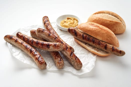 Tasty grilled sausages and fresh bread placed near bowl with sauce against light background