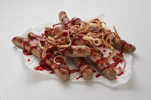 From above of appetizing grilled sausages served with onions and spicy sauce on paper napkin against light background