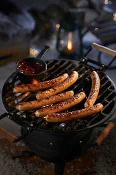 High angle of appetizing grilled sausages with sauce on metal barbecue grid on backyard at night