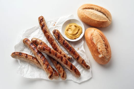 Top view of bowl with sauce placed between delicious grilled sausages and fresh bread against white background in studio
