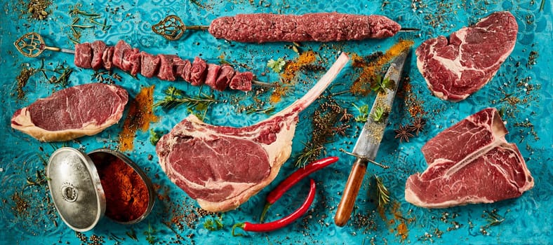 Top view arrangement of fresh raw meat steaks and chili peppers placed on blue table