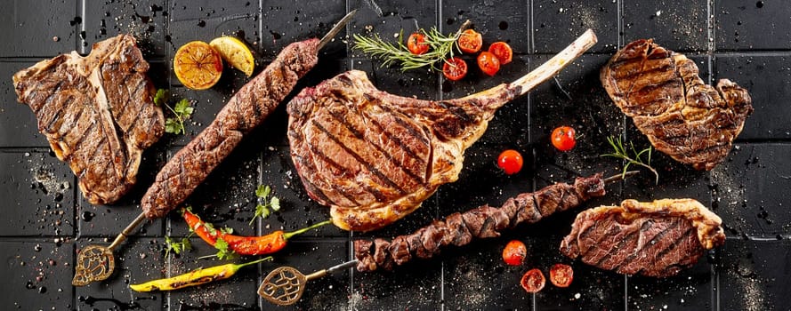 From above of tasty grilled meat steaks placed on black wooden table with spicy red chili peppers and tomatoes